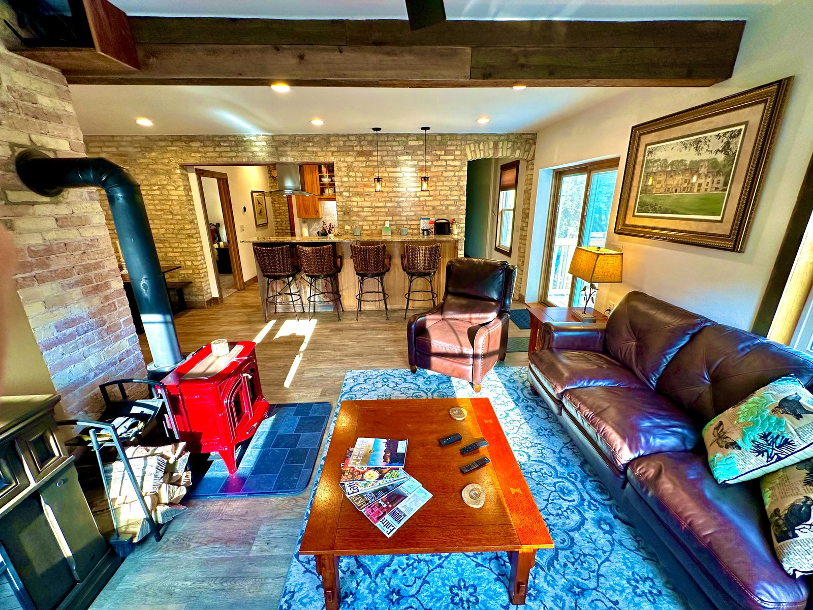 Living room with red wood stove, leather seating, and kitchen bar