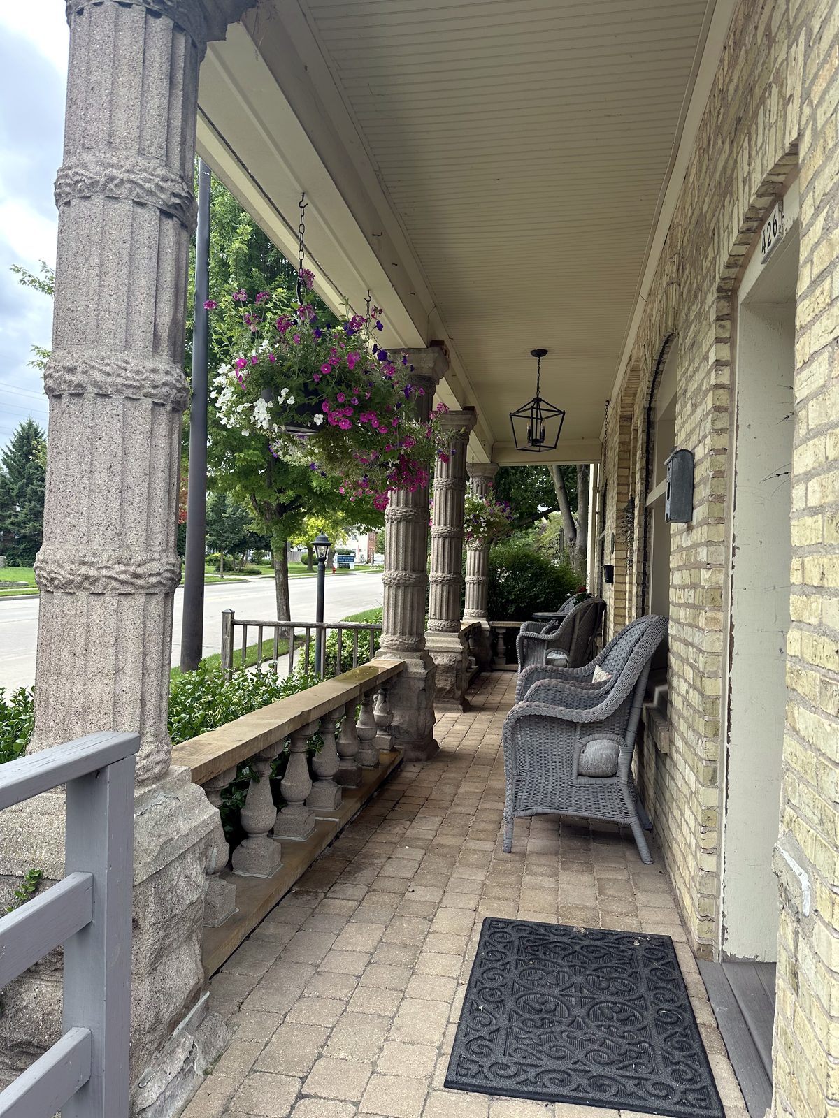 Long view along the historic front porch with columns, chairs, and hanging flowers