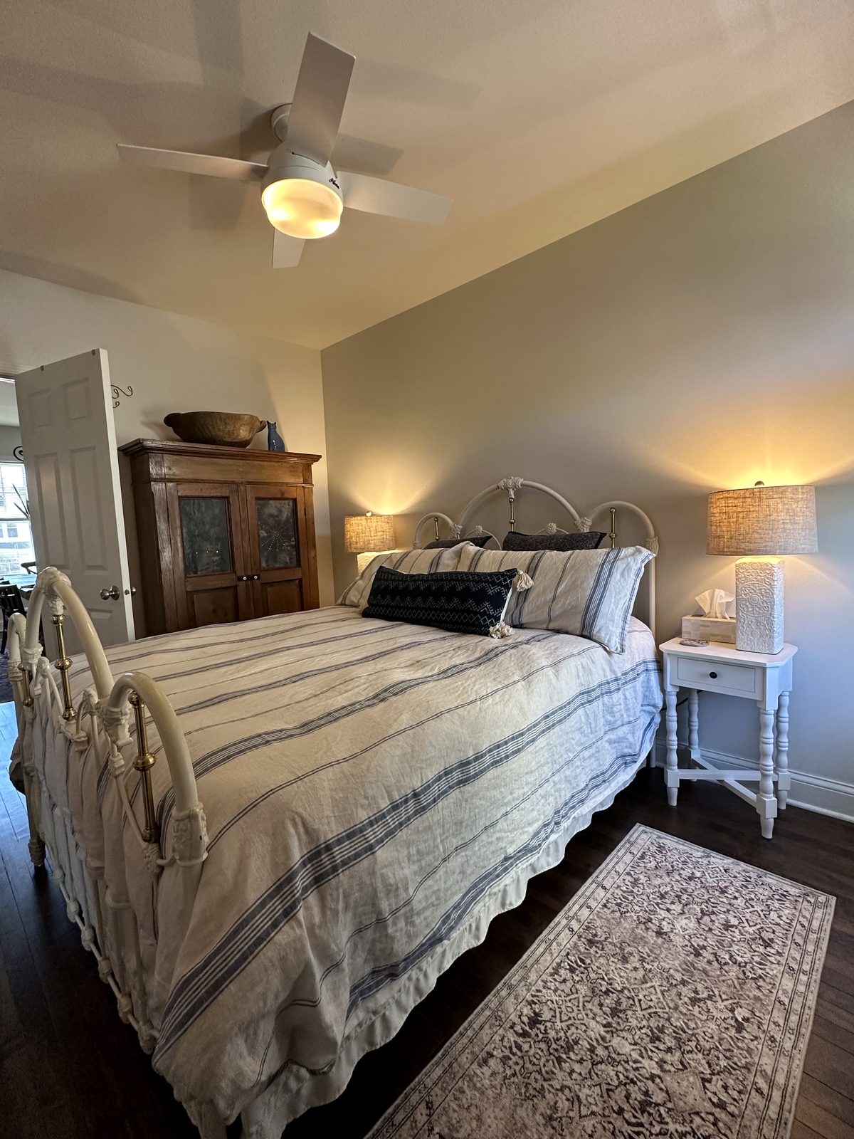 Bedroom with white iron bed, blue-striped linens, and vintage armoire