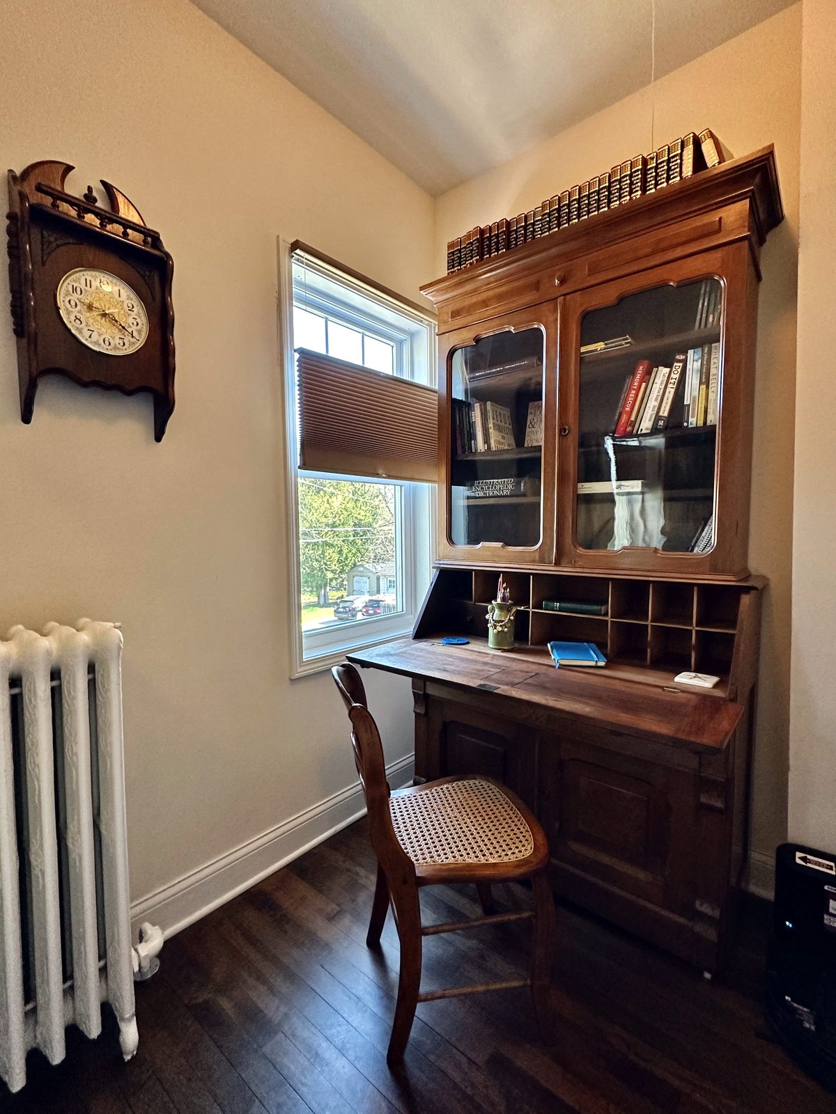 Antique desk with glass-front bookcase beside a window
